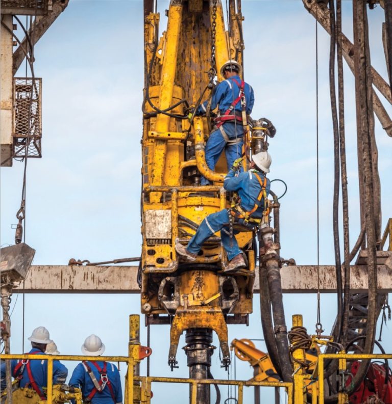 Workers in safety gear operating heavy drilling equipment on a construction site.