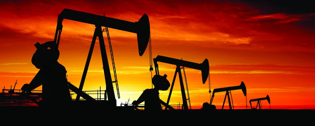 Silhouettes of oil pumpjacks against a fiery sunset sky.