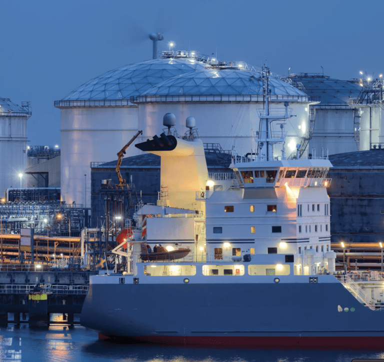 A cargo ship docked at an industrial port during twilight.