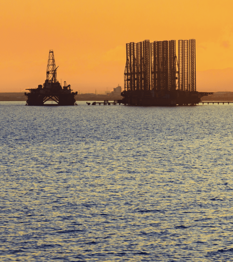Oil rig and support vessel at sunset on calm sea waters.