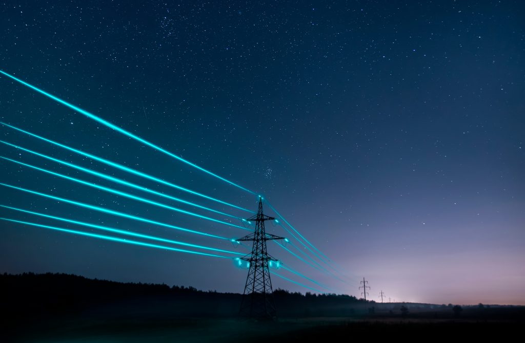 Electricity pylon with glowing blue power lines under a starry night sky.