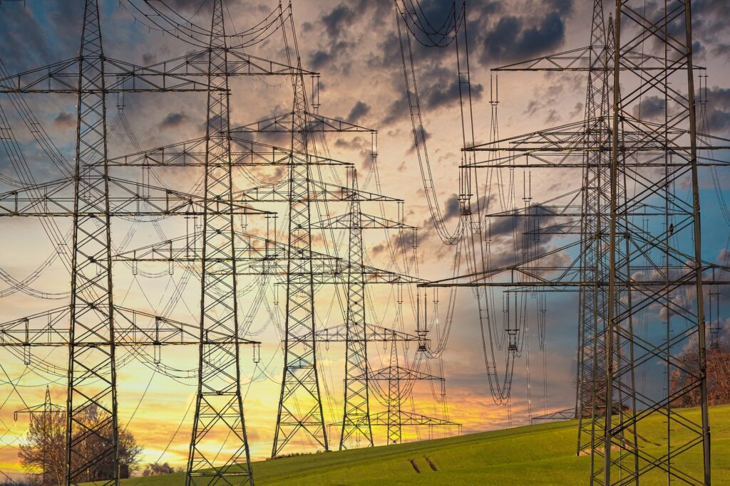 Electricity pylons standing tall against a sunset sky.