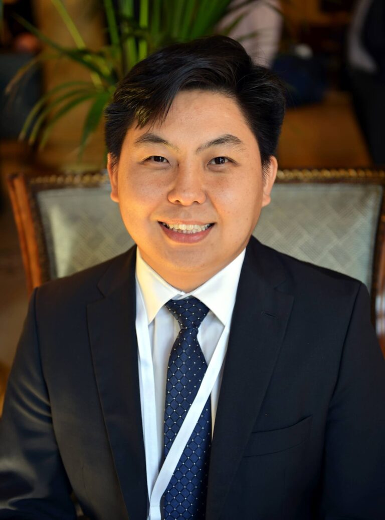 A man in a formal suit and tie smiling at the camera.