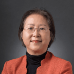 Professional portrait of a confident middle-aged woman wearing glasses and an orange blazer.